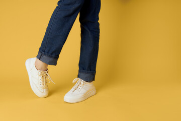 Fashionable shoes white sneakers legs yellow background cropped view