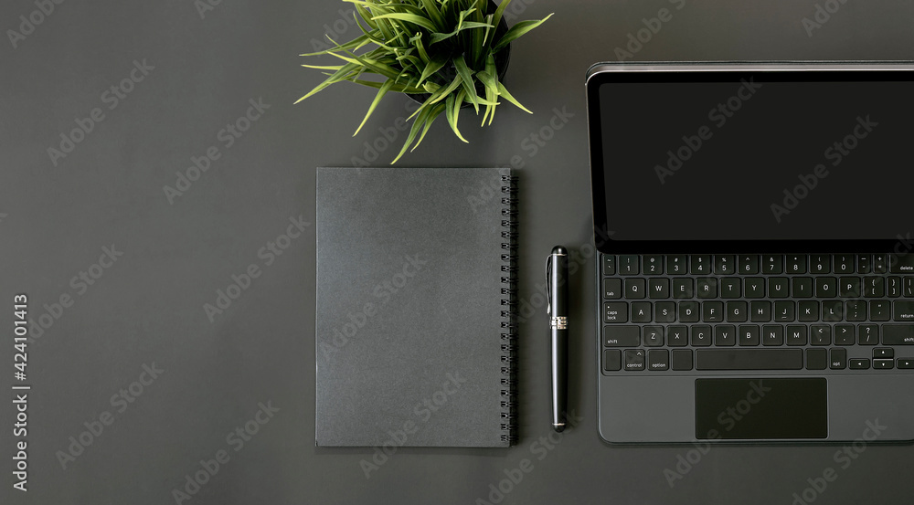 Wall mural mockup top view of tablet with keyboard, notebook, pen and houseplant on black background.