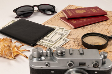 world map, two passports, a magnifying glass, money in a black leather wallet, an old film camera, sunglasses and a shell on a white table. selective focus. inscription - passport Russian Federation