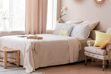 Beautiful and comfortable bedroom in beige colors. The bedroom has a modern bed, an armchair and a bedside stand