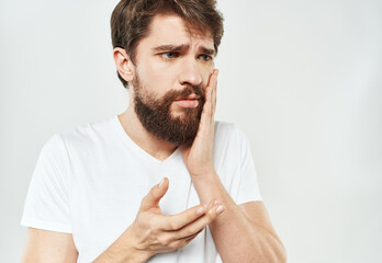 An emotional man in a white T-shirt gestures with his hands on a light background