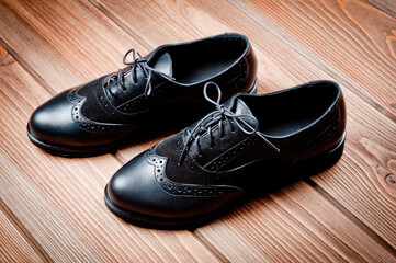 Black imitation leather shoes laced with wide laces. Close-up shot.