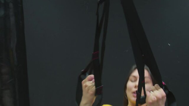 Young fit woman in yellow top doing push ups with trx fitness straps in the gym.