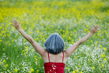 Woman in red dress looking back at field of blooming flowers with arms raised. Springtime, Northern California.