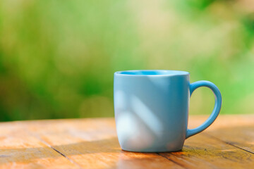 Simple blue ceramic mug on wooden table on green bokeh background. Copy space 