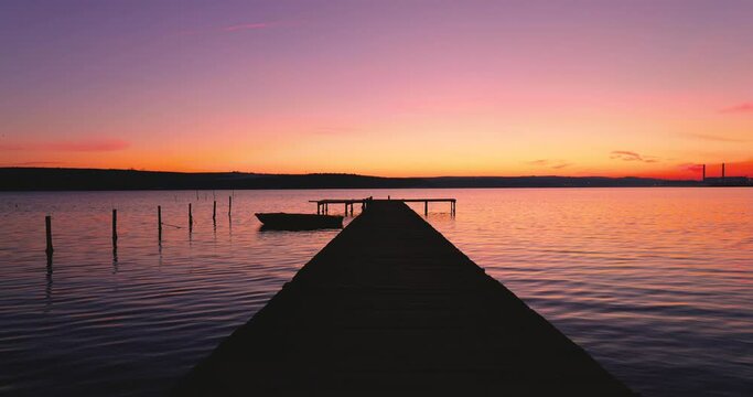Wooden dock on the lake and fishing boat on sunset, 4k video