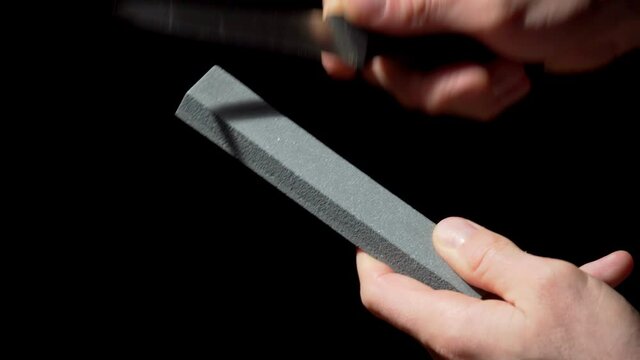 A closeup of hands sharpening a small kitchen knife with a stone.