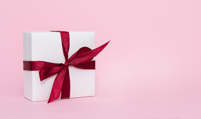 Gift box with red ribbon on pink background