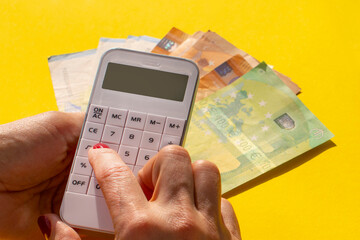 a white calculator in a woman's hand and euro banknotes on a yellow background