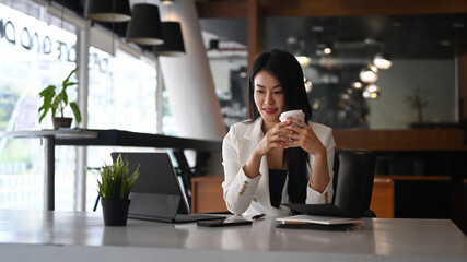 Young woman entrepreneur holding coffee cup and reading news computer tablet at the morning.