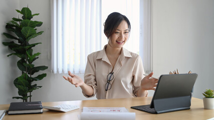 Happy young businesswoman using tablet computer making video conference with her colleagues at her workplace.