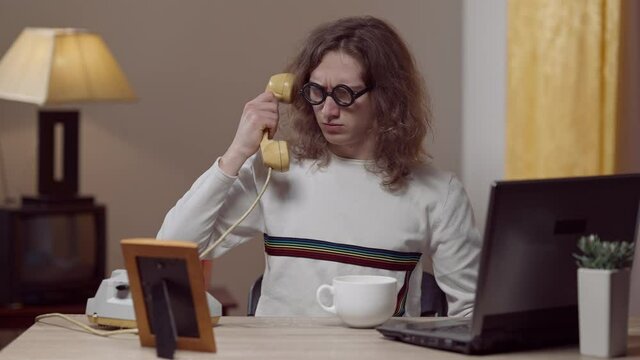Confident nerd young man putting on retro eyeglasses and picking up phone. Middle shot portrait of Caucasian guy holding telephone handset with someone yelling in it. Stress in 1980s 1990s.