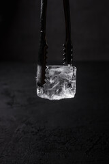 A clear hoshizaki ice cube in bartender ice tongs, dark backdrop