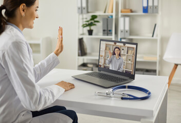 Online doctor greeting female patient in an online video meeting. General practitioner waving hand...