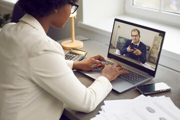 Young employee having online work meeting with senior boss, over shoulder view. Two multiethnic...