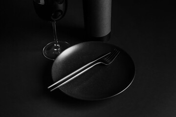 Stylish table setting with glass and bottle of wine on dark background