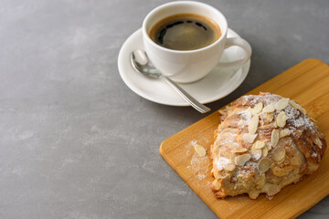 Almond croissant on wooden board with black coffee on concrete grey background
