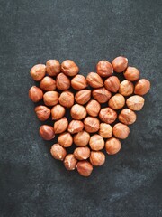 Heart shaped white plate with different dried fruits and nuts on black background. Healthy food and snack. Flat lay. Copy space text
