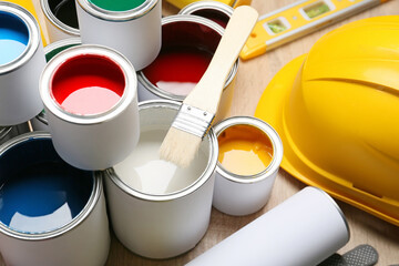 Cans of paints and tools on light wooden background