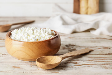 Bowl with cottage cheese on light wooden background