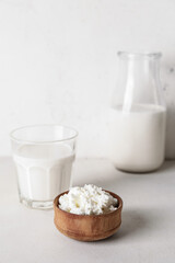 Bowl with cottage cheese and glass of milk on light background