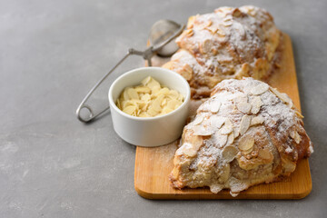 Almond croissant on wooden board with powdered sugar and almond petals