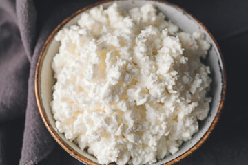 Bowl with cottage cheese on dark background, closeup
