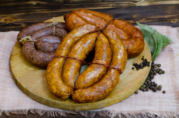 A set of traditional homemade smoked and raw sausages on a round wooden board. Dark wooden rustic background. Copy space