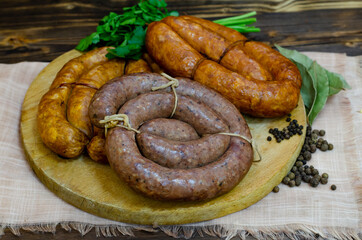 A set of traditional homemade smoked and raw sausages on a round wooden board. Dark wooden rustic background. Copy space