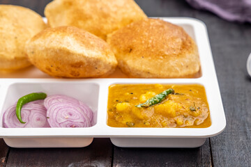 Masala Aloo Sabzi or Indian potato curry served with fried puri or Poori with sliced onion and mango pickle on a white plate  