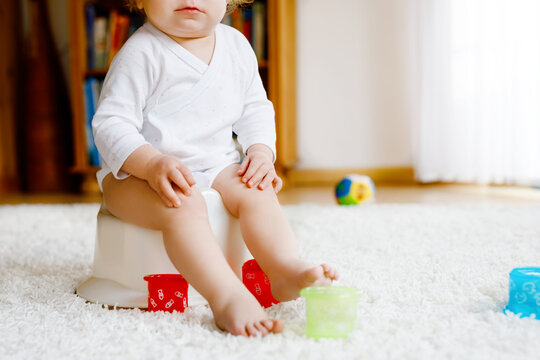 Closeup of cute little old toddler baby girl child sitting on potty. Kid playing with educational toy and Toilet training concept. Baby learning, development steps. No face, unrecognizable person.