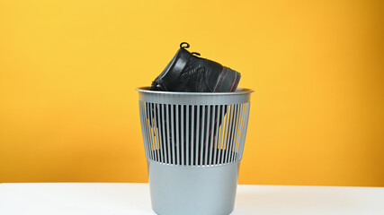 A man throws a pair of leather shoes into a plastic bucket on yellow background. Conscious consumption concept