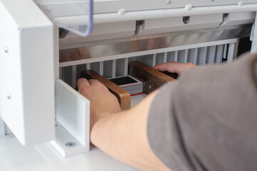 two man hands align a stack of business cards or tags with wooden pushers in an automatic paper cutting machine, a professional cutter, equipment for a printing house or workshop.