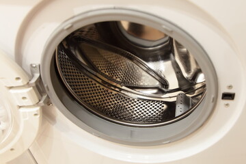 Front loaded slim washing machine empty can inside with shiny stainless steel rotor drum without water close-up