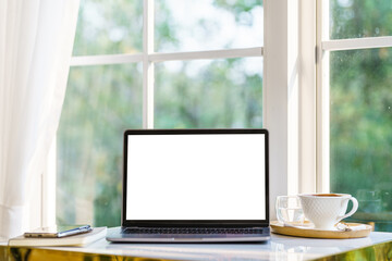 Mockup of laptop computer with empty screen with notebook,coffee cup and smartphone on table side the window in the coffee shop at the cafe,White screen
