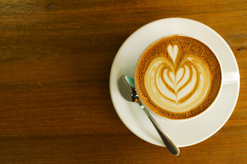 Hot coffee latte with latte art milk foam in cup mug on wood desk on top view. As breakfast In a coffee shop at the cafe,during business work concept