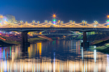 Fototapeta premium Beautiful light on the Nan River at night on the bridge (Naresuan Bridge) on the Road in Realm for Naresuan the Great Festival and Red Cross Annual event in Phitsanulok,Thailand.