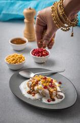 woman garnishing or serving Dahi Bhalla or Dahi Vada with tamarind sauce, pomegranate seeds, and boondi
