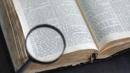 Obraz premium Opening ancient bible book, text read through magnifying glass. Search for truth and meaning of life. Russia, 27.12.2020