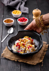 woman garnishing or serving Dahi Bhalla or Dahi Vada with tamarind sauce, pomegranate seeds, and boondi