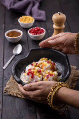 woman garnishing or serving Dahi Bhalla or Dahi Vada with tamarind sauce, pomegranate seeds, and boondi