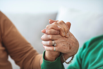 Closeup of an old caucasian man and an old caucasian woman sitting in a couch holding hands with affection. Cropped shot of a senior couple holding hands