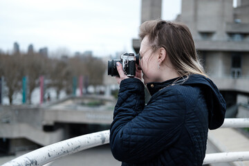 Young woman taking pictures with a vintage film camera in riverside London.