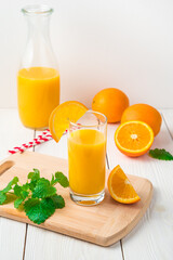 Orange juice with a glass and mint do not appear on a light background with a decanter. Side view, vertical.