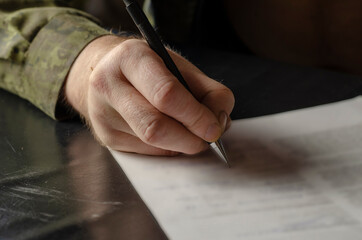 A middle-aged adult man in a green camouflage uniform signs a do