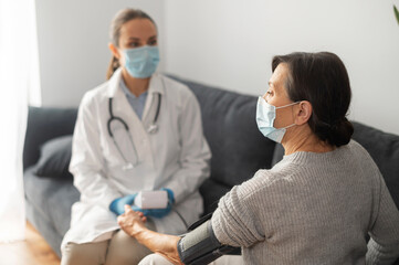 Nurse wearing mask caring about elderly female patient at home during pandemic period, the doctor...