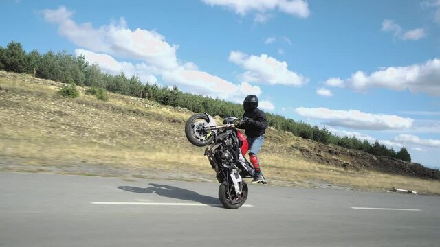Biker man making a stunt, driving the motor cycle on the back wheel only, extreme driving