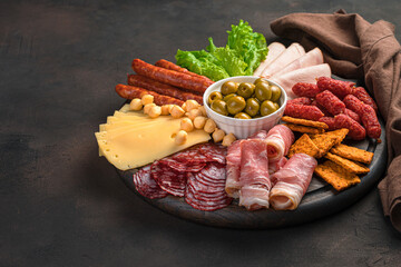 Meat and cheese delicacies with herbs and olives on a brown background.