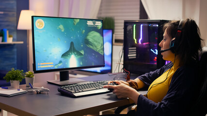 Fototapeta premium Pro player talking into microphone with other players for space shooter tournament. Gamer using wireless joystick for online championship on powerful computer late at night in gaming room