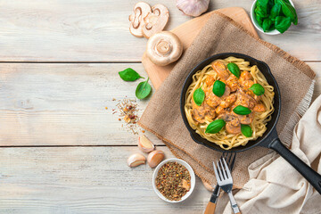 Pasta with mushrooms and basil in a frying pan on a light background.